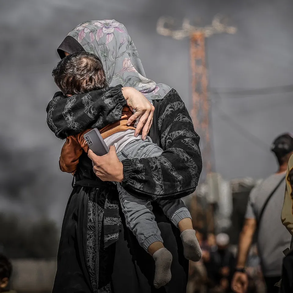 Woman in Gaza cradles her young child amidst Israeli destruction