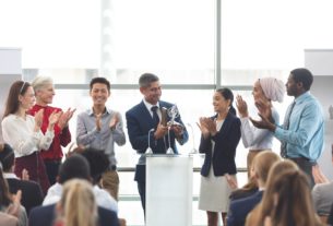 Businessman holding award on podium with colleagues at business seminar